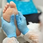 woman hands in gloves massage the feet with a pedicure, smear cream on the foot. Foot care salon, doctor podiatrist treatment office